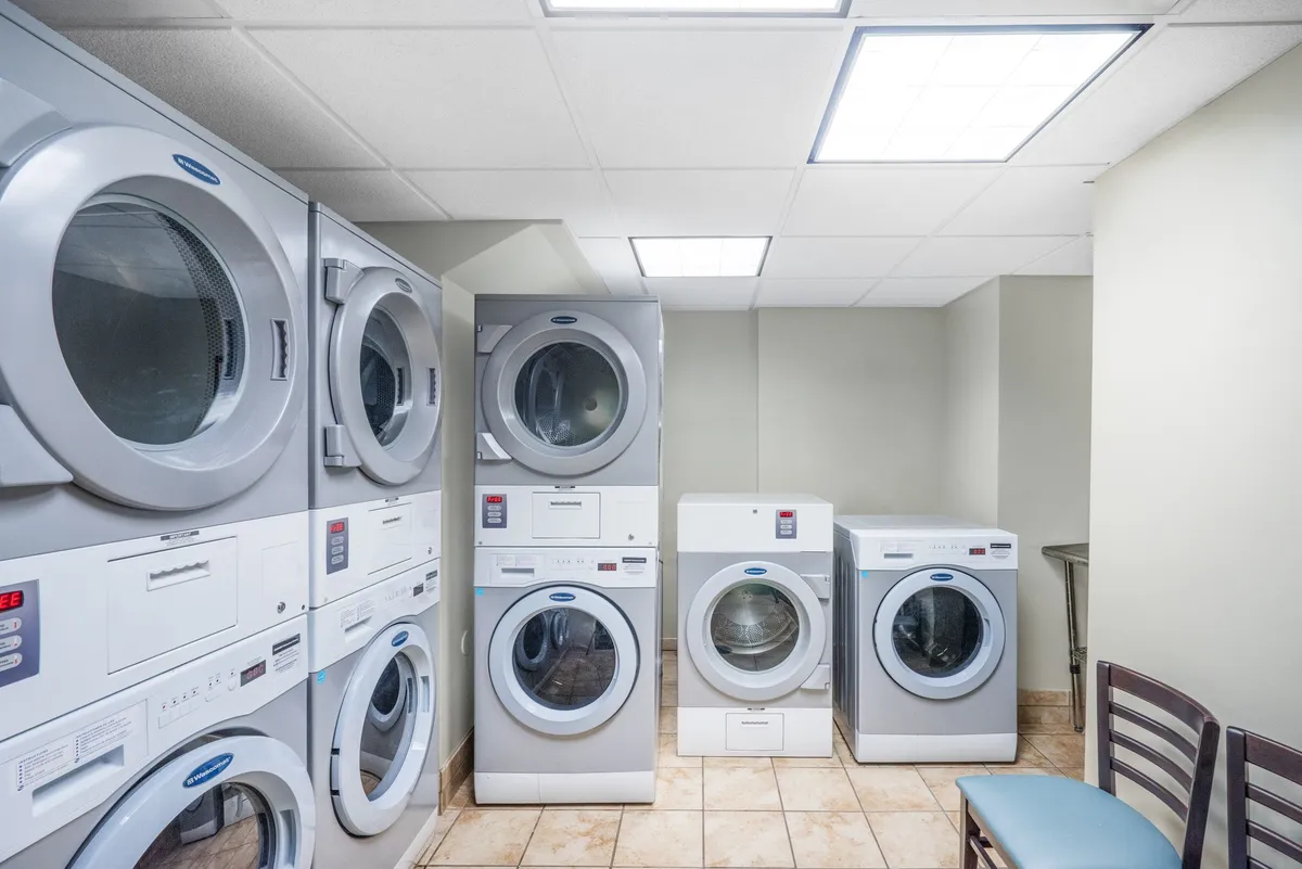 A practical laundry area with multiple stacked washing machines and a single drying machine, complemented by a seating area for guests to wait comfortably. The space is clean and functional, emphasizing convenience and community.